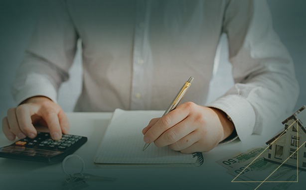 Person calculating and writing at a desk with a house model, money, and keys.