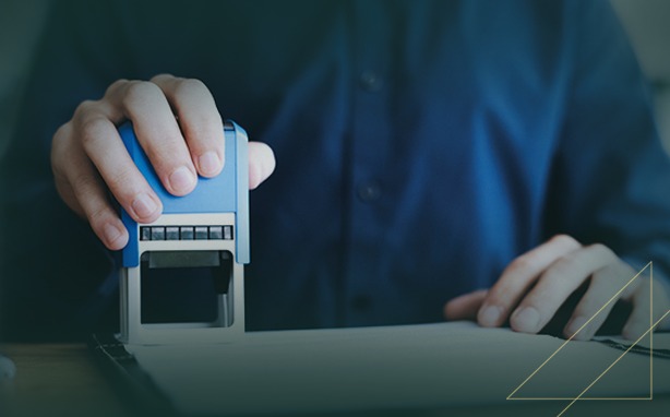 Person stamping a document with a blue and silver self-inking stamp on a wooden desk.