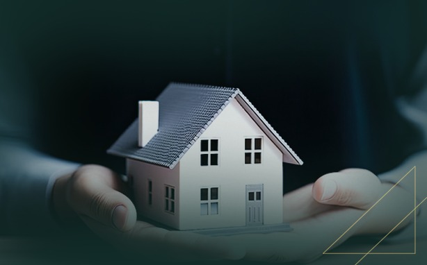 Hands holding a miniature white house with a dark gray roof.