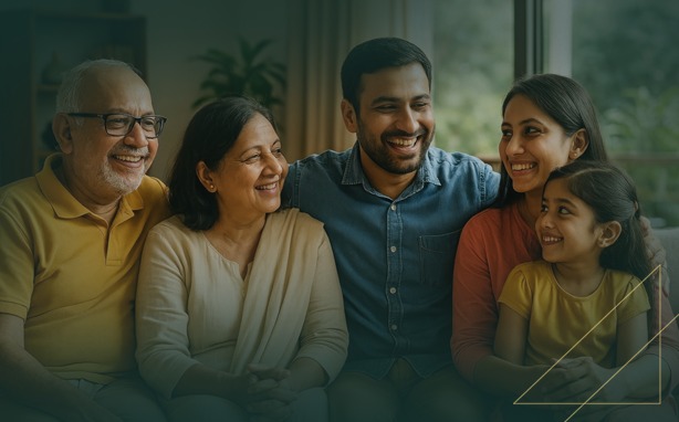 Multi-generational family of five smiling on a couch. Two elders, a man and a woman, and a younger couple with a child.